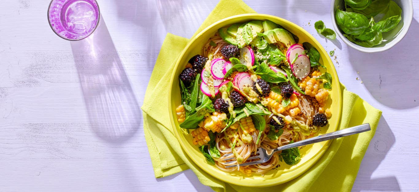 Easy Gourmet Noodle Bowls με βατόμουρα, φρέσκο καλαμπόκι, και αβοκάντο-ασβέστη ντύσιμο σε μια κίτρινη χαρτοπετσέτα σε ένα φόντο λιλά