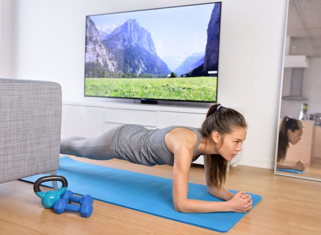 Living Room Fitness Workout - Κορίτσι που κάνει ασκήσεις σανίδων για να ασκήσει πυρήνα στο σπίτι. Οι νεαροί ασιατικοί μύες που εκπαιδεύουν τη γυναίκα μπροστά από την τηλεόραση ως μέρος ενός υγιεινού τρόπου ζωής χωρίς να πηγαίνουν στο γυμναστήριο.