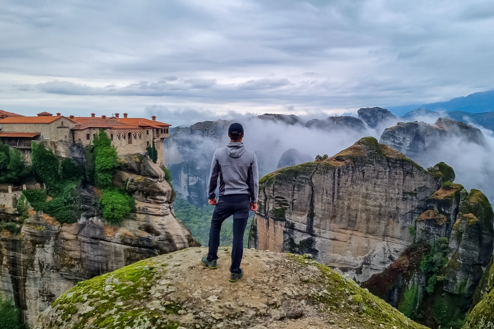 Meteora, Ελλάδα Ένας άνδρας στέκεται κοντά στην άκρη του βράχου με θέα ένα μοναστήρι στη μετεωραία της Ελλάδας