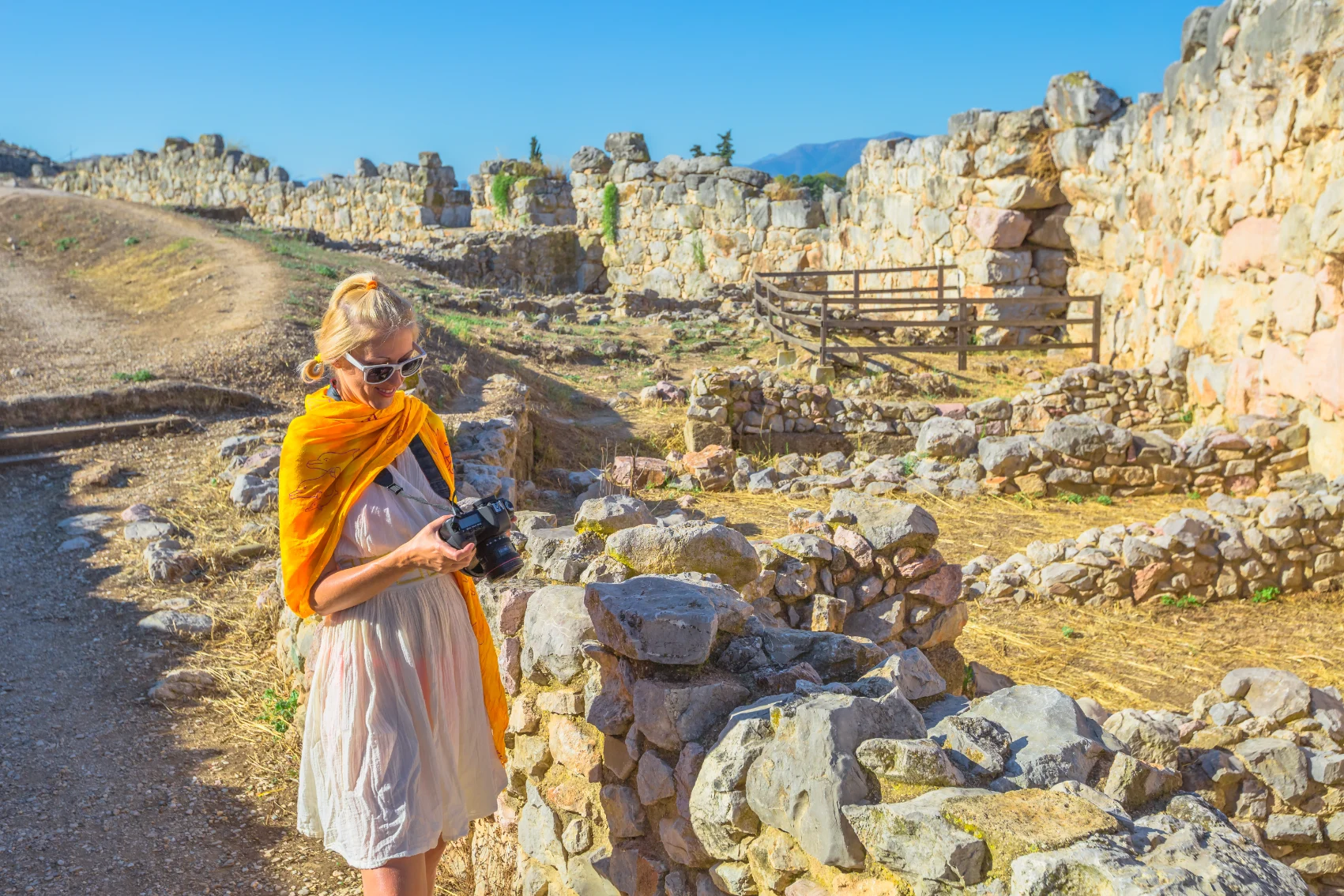 Mycenae, Ελλάδα Μια γυναίκα ταξιδιώτης κοιτάζει την κάμερά της ενώ περπατάει μέσα από τα ερείπια των αρχαίων μυκήνων της Ελλάδας